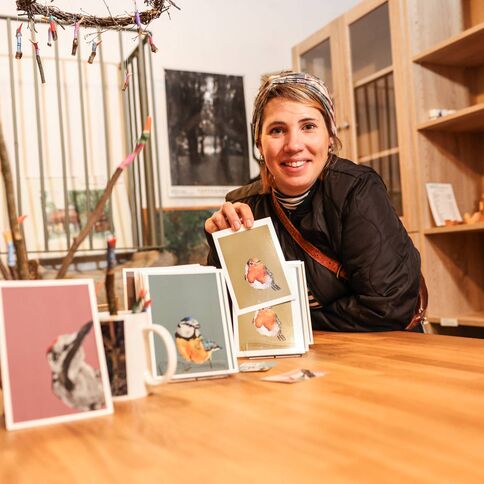 Eine lächelnde Frau präsentiert Kunstkarten im Tuppenhof in Kaarst auf einem Holztablett.