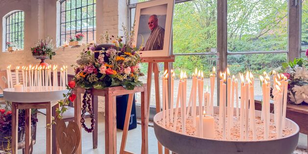 Viele brennende Kerzen und bunte Blumen schmücken eine Gedenkstätte mit einem Foto von Stevens in einem hellen Raum.