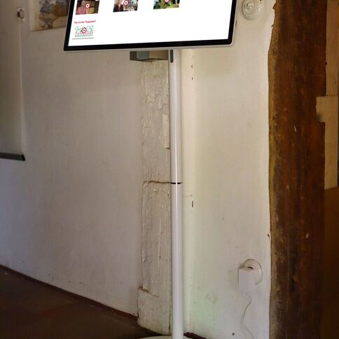 Ein Touchscreen-Mediensäule zeigt Inhalte von Tuppenhof in Kaarst, integriert in eine historische Umgebung.