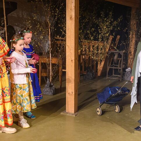 Drei Mädchen in bunten Kleidern stehen neben einer Frau mit einem Einkaufswagen bei einer Aufführung im Tuppenhof in Kaarst.