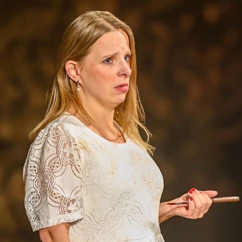 Eine Frau in einem weißen Spitzenkleid hält nachdenklich einen Stift, möglicherweise bei einer Veranstaltung im Tuppenhof Kaarst.