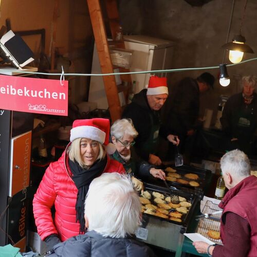 Menschen in weihnachtlicher Stimmung bereiten Reibekuchen in einer gemütlichen, festlich dekorierten Umgebung zu.