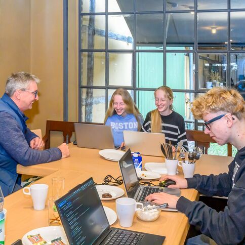 Vier Personen arbeiten und lachen gemeinsam an Laptops in einem gemütlichen Raum im Tuppenhof in Kaarst.