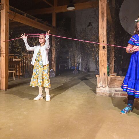 Drei Mädchen in bunten Kleidern spielen mit rotem Garn im Tuppenhof in Kaarst.