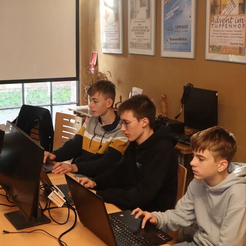 Drei Jugendliche arbeiten konzentriert an Laptops in einem Raum mit Tuppenhof-Postern an der Wand in Kaarst.