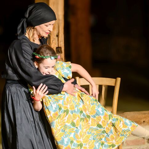 Eine Frau in traditioneller Kleidung umarmt ein fröhliches Mädchen in einem bunten Kleid am Tuppenhof in Kaarst.