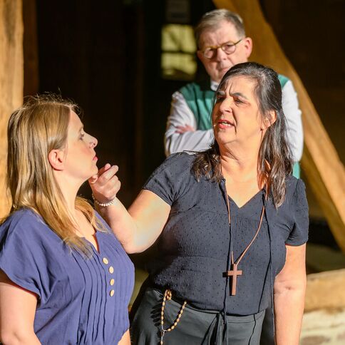 Eine Frau spricht ernst mit einer jüngeren Frau im Tuppenhof Kaarst, während ein Mann im Hintergrund zusieht.