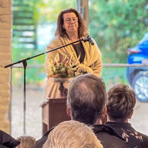 Eine Frau spricht am Rednerpult vor einem Publikum, während ein blaues Auto draußen geparkt ist. | © Nancy Stevens
