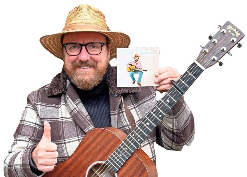 Ein Mann mit Strohhut hält eine Akustikgitarre und eine CD, während er lächelnd den Daumen hebt.