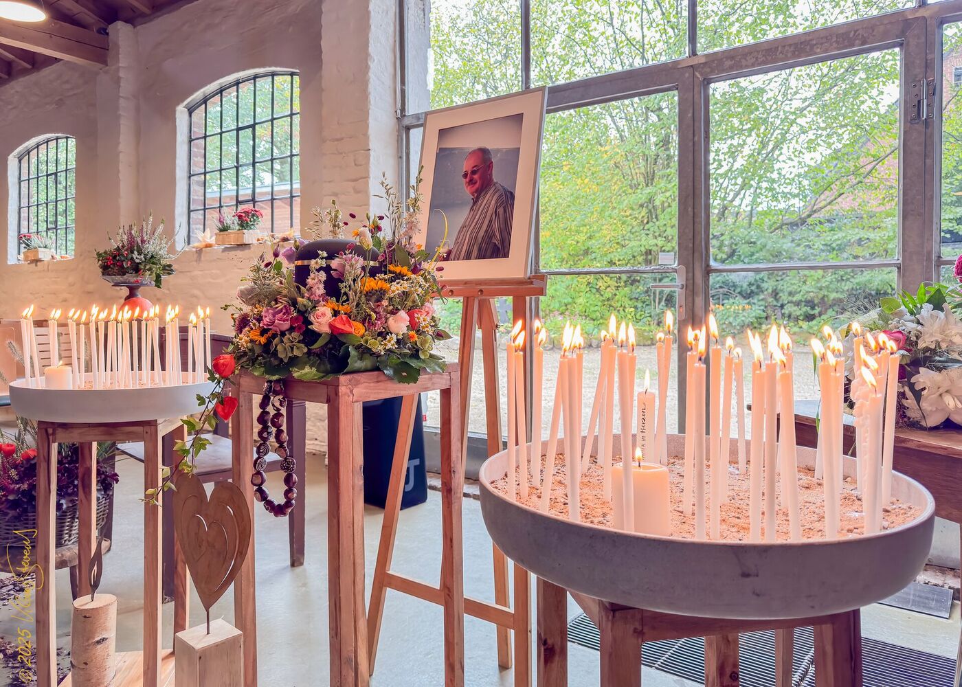 Viele brennende Kerzen und bunte Blumen schmücken eine Gedenkstätte mit einem Foto von Stevens in einem hellen Raum.