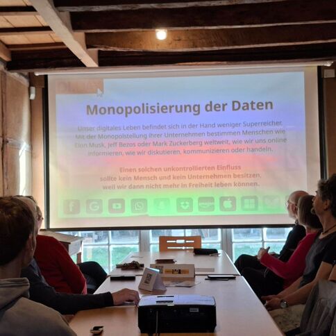 Eine Gruppe von Personen in Tuppenhof, Kaarst, diskutiert über die Monopolisierung von Daten, während ein Vortrag läuft.