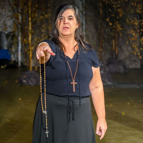 Eine Frau zeigt mit einem Rosenkranz in der Hand auf etwas, während sie im Tuppenhof in Kaarst steht.