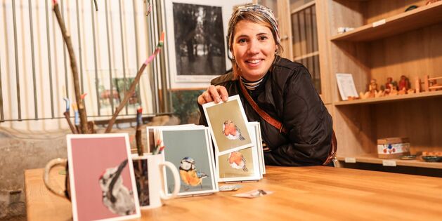 Eine lächelnde Frau präsentiert Kunstkarten im Tuppenhof in Kaarst auf einem Holztablett.