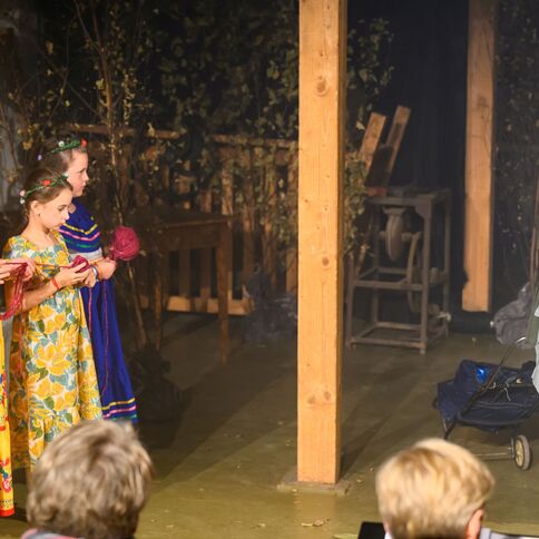 Drei Kinder in bunten Kleidern stehen auf der Bühne des Tuppenhofs in Kaarst und halten rote Wolle.