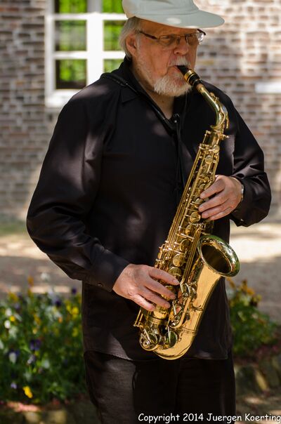 Ein Musiker spielt Saxophon im Tuppenhof Kaarst, umgeben von bunten Blumen und einer entspannten Atmosphäre.