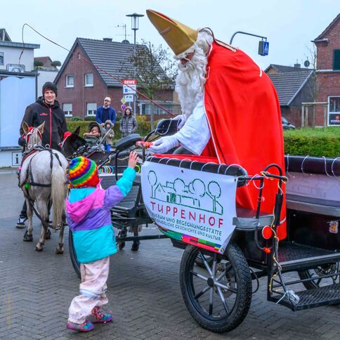 Ein Kind in bunter Kleidung begrüßt den Nikolaus auf einem festlich geschmückten Wagen vor dem Tuppenhof in Kaarst.