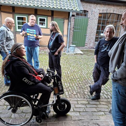Eine Gruppe von Männern unterhält sich lebhaft im Tuppenhof in Kaarst, während eine Frau im Rollstuhl aufmerksam zuhört.