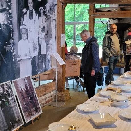 Besucher erkunden die Ausstellung im Tuppenhof Kaarst mit historischen Fotos und Geschirr auf einem langen Tisch.