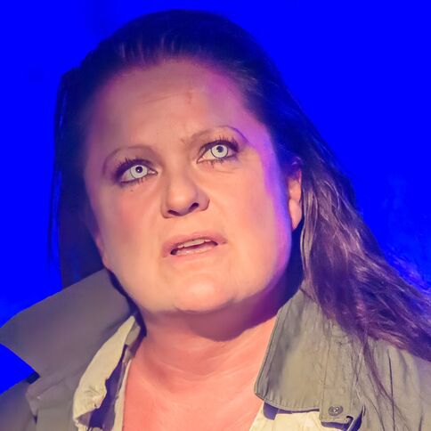 Eine Frau mit ausdrucksstarkem Blick steht im blauen Licht bei einer Veranstaltung im Tuppenhof in Kaarst.