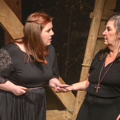 Zwei Frauen in schwarzer Kleidung diskutieren lebhaft in einer Holzkulisse bei Tuppenhof Kaarst.