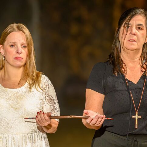 Zwei Frauen in Kaarst halten gemeinsam eine Holzplatte und wirken nachdenklich im historischen Ambiente des Tuppenhofs.