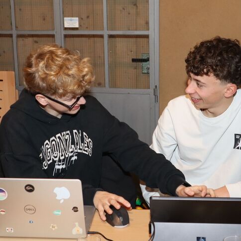 Zwei junge Männer lachen herzlich am Tisch mit Laptops im Tuppenhof in Kaarst.