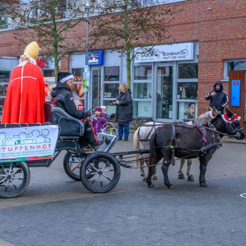 Ein Festumzug mit einer Kutsche, gezogen von Ponys, zieht durch Kaarst, während ein Banner für Tuppenhof wirbt.
