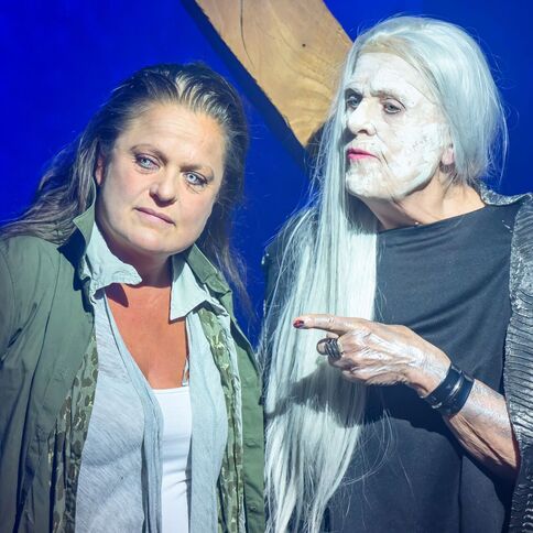 Zwei Menschen stehen in einem dramatischen Bühnenlicht im Tuppenhof Kaarst, eine Person mit weißem Haar deutet auf die andere.