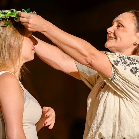 Eine Frau legt einer anderen eine Blumenkrone auf den Kopf, ein feierlicher Moment auf dem Tuppenhof in Kaarst.