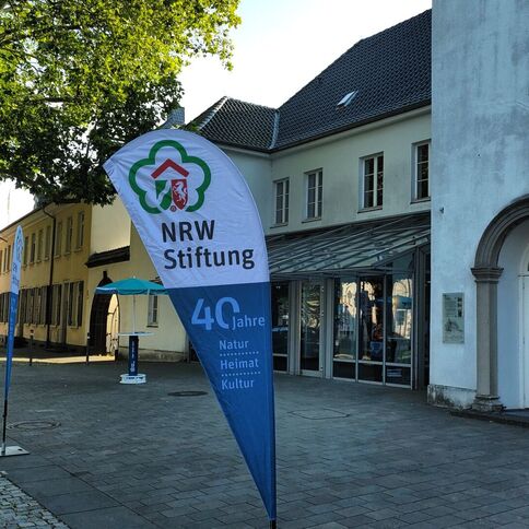 Ein Banner der NRW Stiftung in Kaarst zeigt 40 Jahre Natur, Heimat und Kultur vor den historischen Gebäuden.