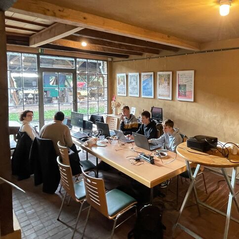 Menschen arbeiten gemeinsam an Laptops in einem rustikalen Raum im Tuppenhof in Kaarst.