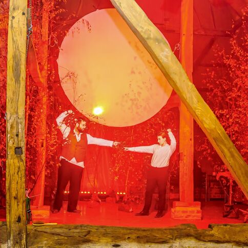 Zwei Männer duellieren sich in einer rot beleuchteten Szene im Tuppenhof Kaarst, umgeben von herbstlichen Bäumen.