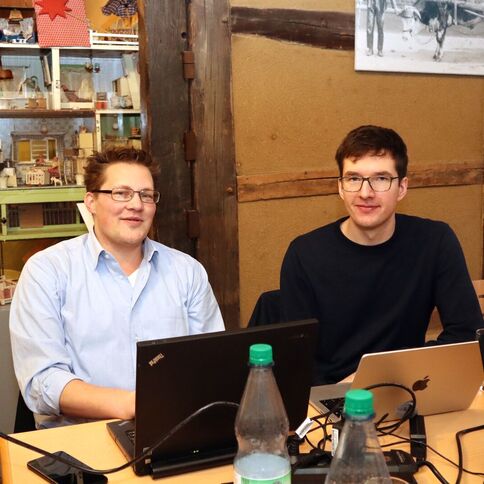 Zwei Männer arbeiten an Laptops in einem gemütlichen Raum im Tuppenhof, Kaarst, umgeben von rustikaler Dekoration.