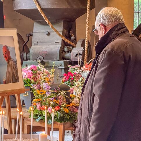 Ein Mann betrachtet ein gerahmtes Foto neben Blumen und Kerzen bei einer Gedenkveranstaltung.