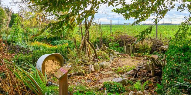 Ein idyllischer Gartenpfad führt durch üppiges Grün und bunte Blumen in eine weite Landschaft.