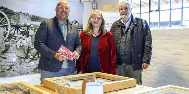 Drei Personen stehen im Tuppenhof, umgeben von Ausstellungsstücken und historischen Fotos aus Kaarst.