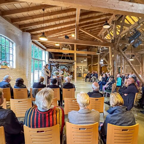 In einem rustikalen Veranstaltungsraum hält ein Redner vor einem interessierten Publikum einen Vortrag.