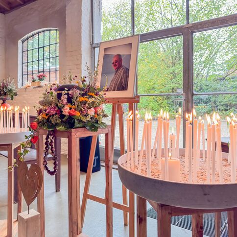 Viele brennende Kerzen und bunte Blumen schmücken eine Gedenkstätte mit einem Foto von Stevens in einem hellen Raum.