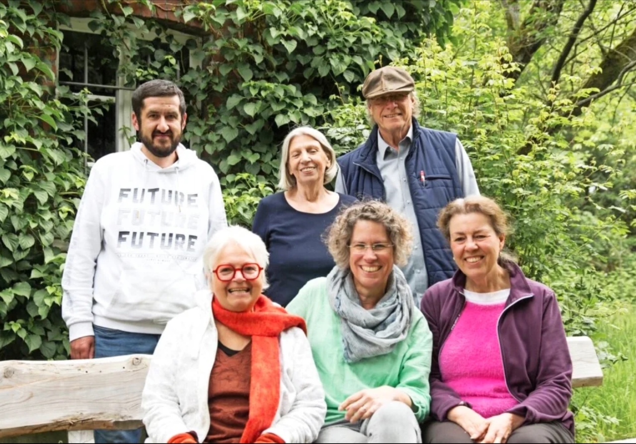 Gruppe von sechs Personen posiert lächelnd im Tuppenhof, Kaarst, umgeben von grüner Natur.